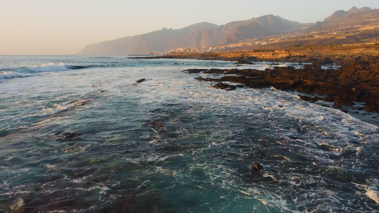 近距离无人机在海洋水面上飞行。海浪起泡沫。在温暖的夕阳下，Los Gigantes悬崖的景色。一望无际碧蓝的天空。视频素材