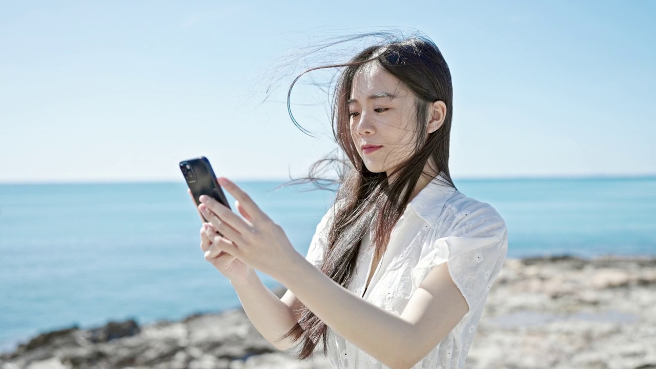 年轻的中国女子在海边用智能手机拍摄微笑视频视频素材