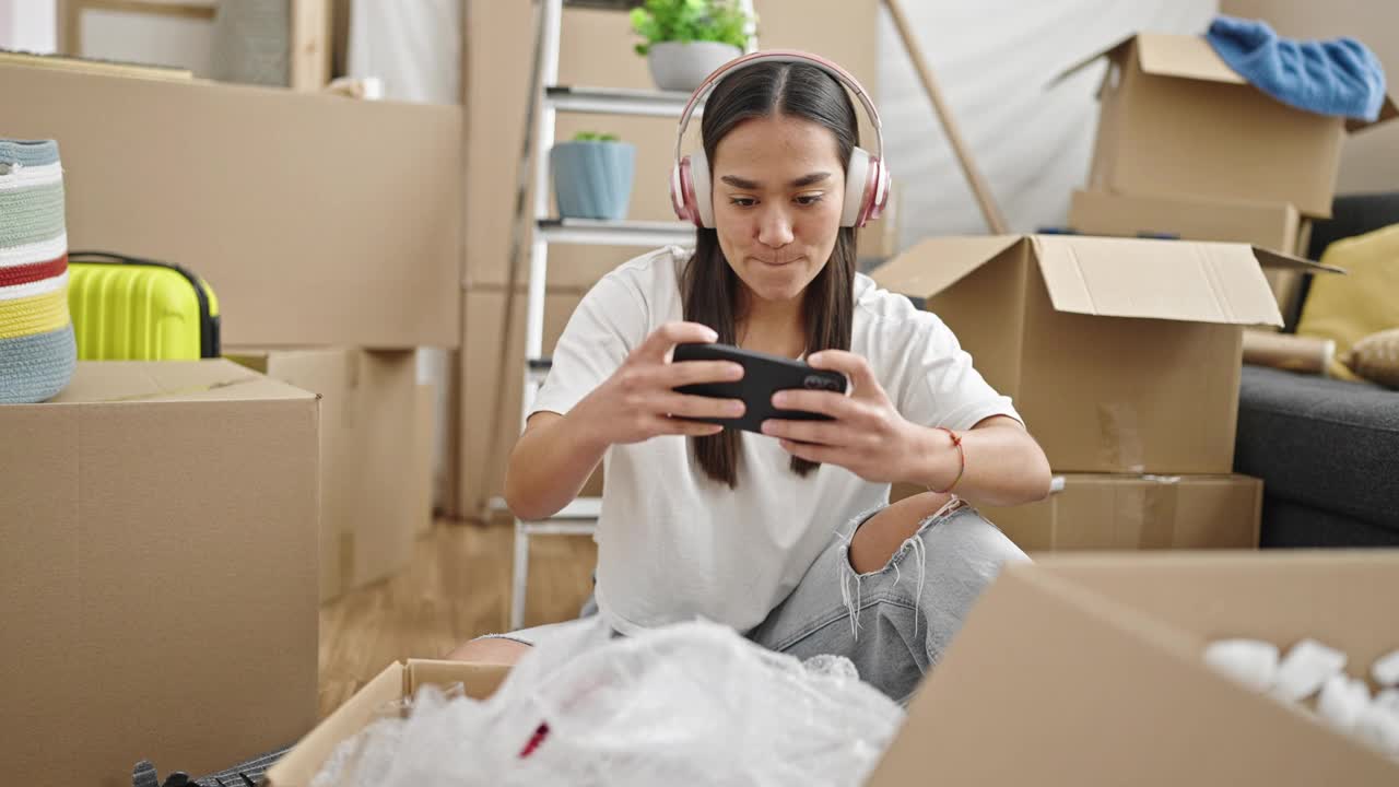 年轻漂亮的西班牙女人在新家用智能手机玩电子游戏视频素材