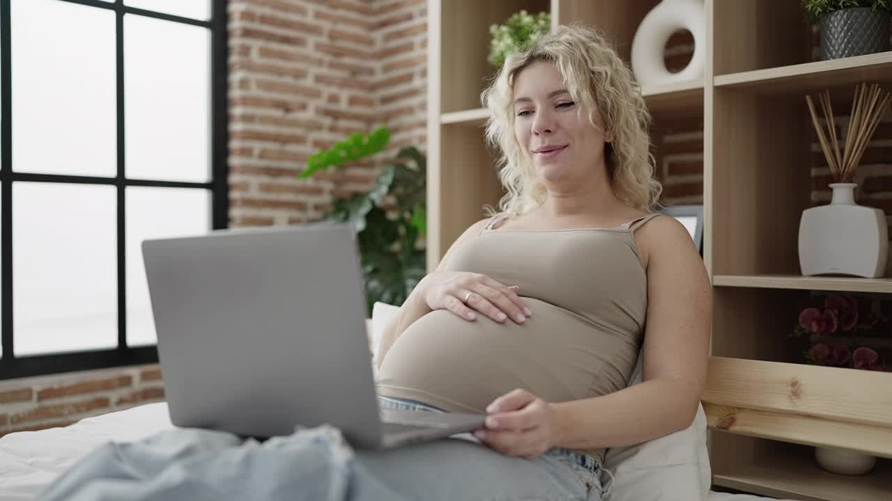 年轻孕妇在卧室里视频通话摸肚子视频素材