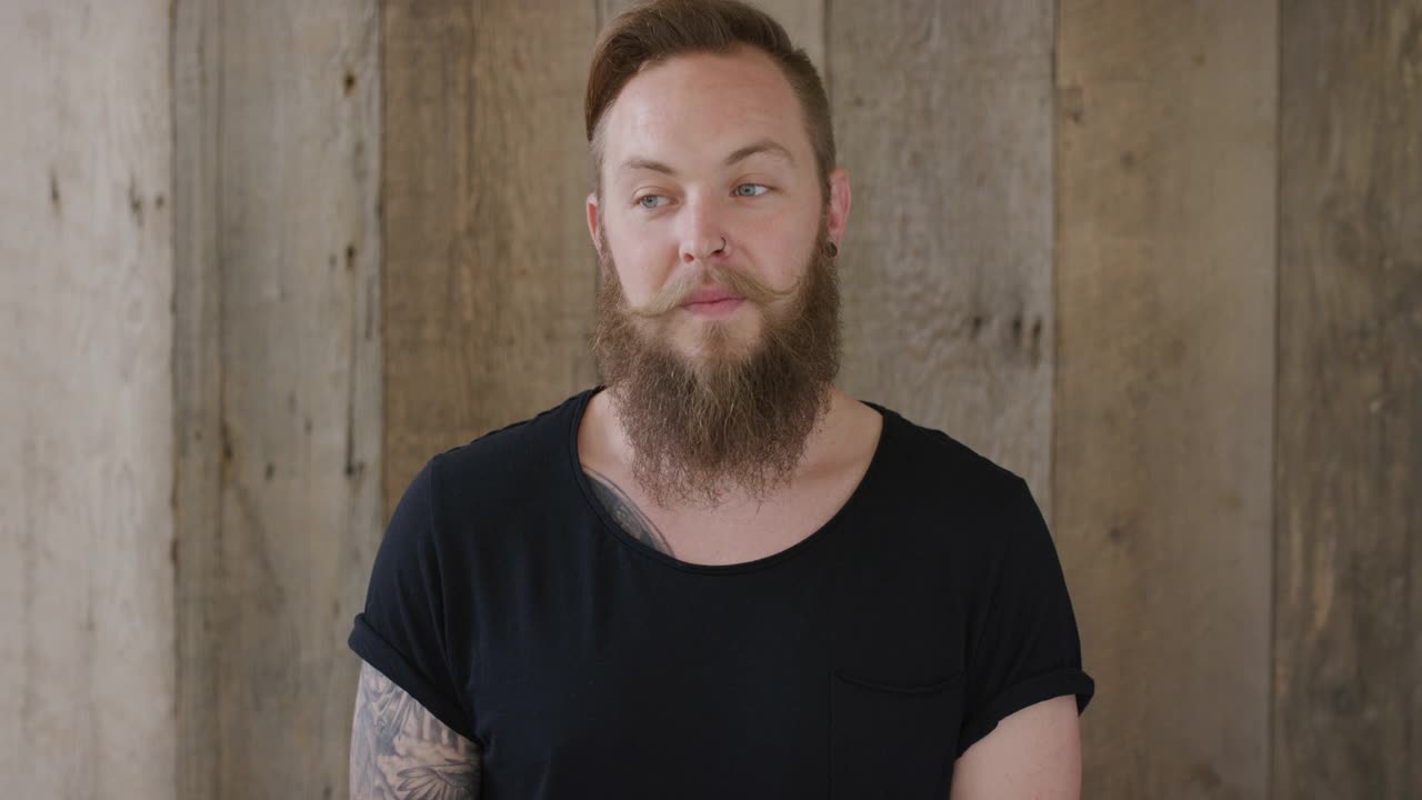 年轻的嬉皮士朋克男子触摸胡子看起来沉思迷人的白人男性木制背景视频素材