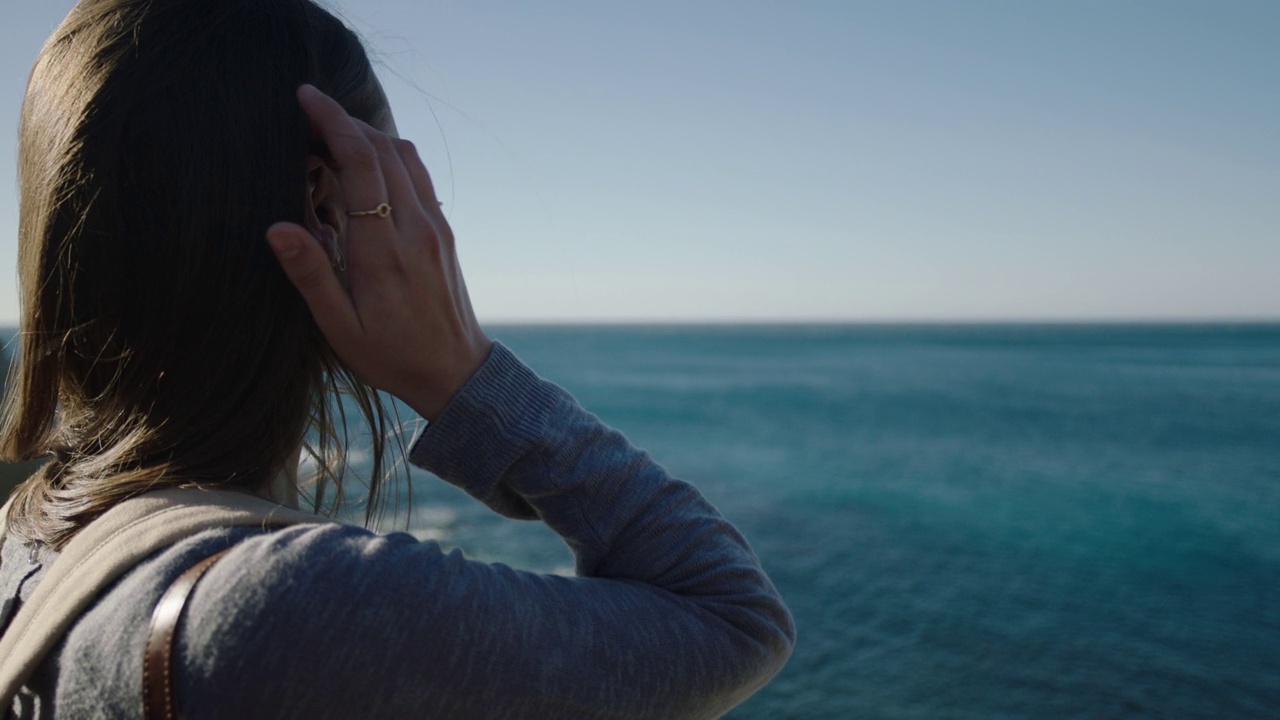 年轻的冒险女人看着美丽的海边景色，享受成功的假期旅行，手穿过头发视频素材