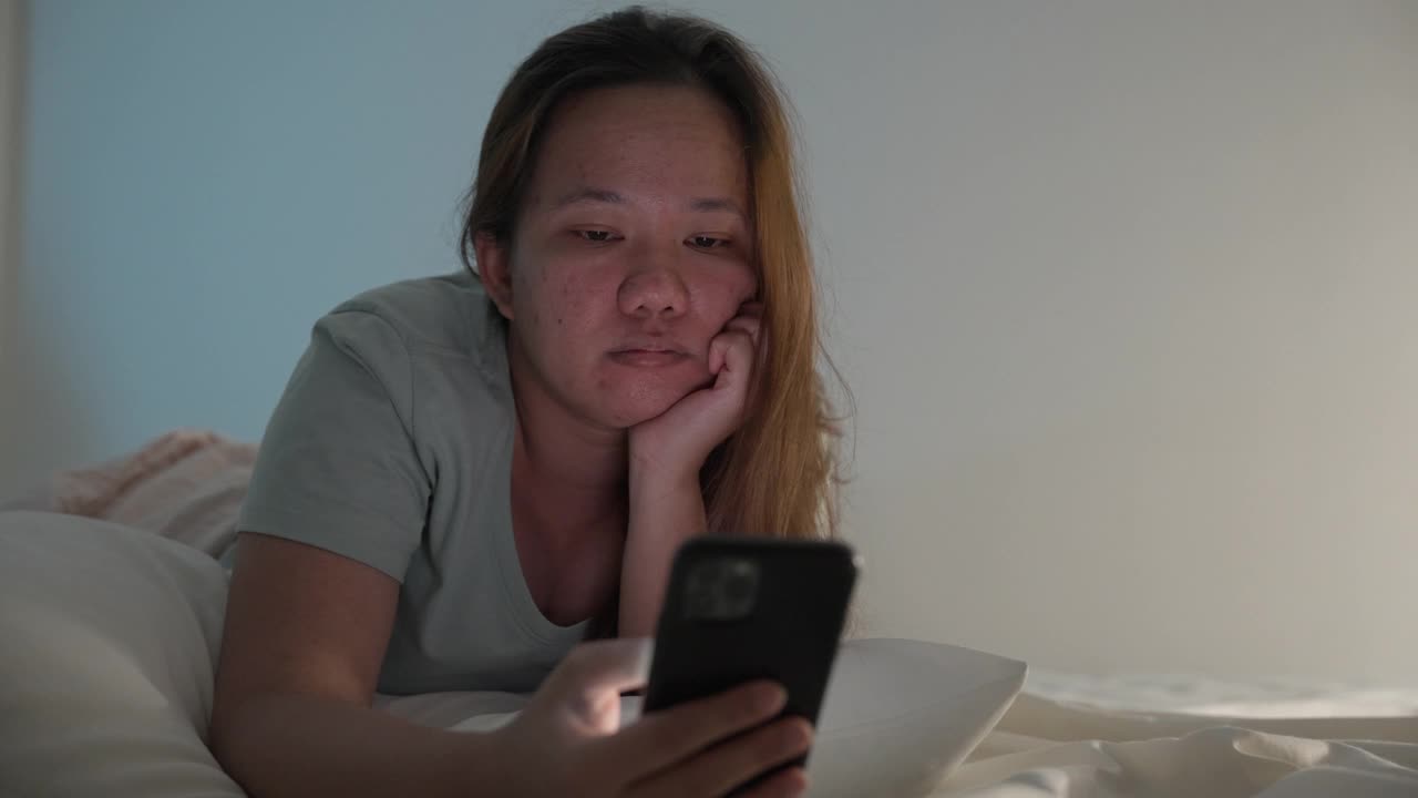 不高兴的亚洲女人晚上在床上玩手机视频素材