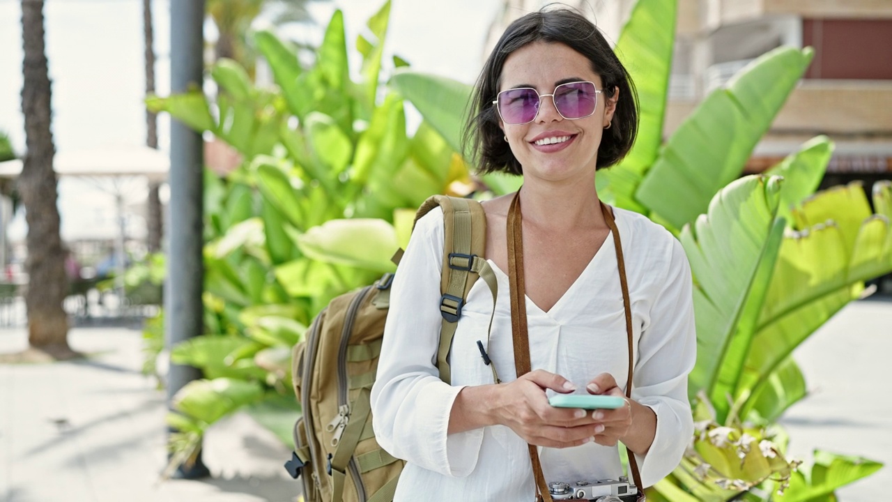 年轻美丽的西班牙女游客在公园里用智能手机自信地微笑着视频素材