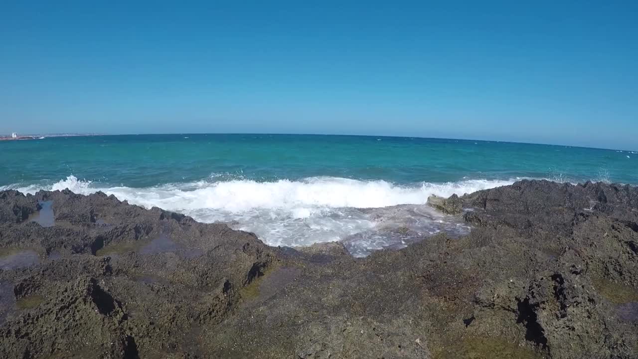 泡沫般的海浪冲击着岸边的岩石，背景是地平线视频素材