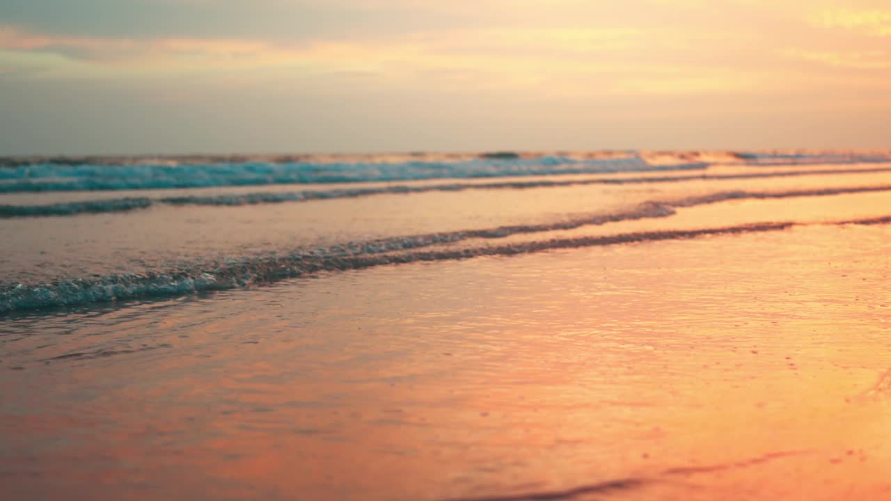 特写-夕阳下柔软的泡沫海浪冲刷着金色的沙滩，海浪在阳光下翻滚到沙滩，假日休闲的概念视频素材