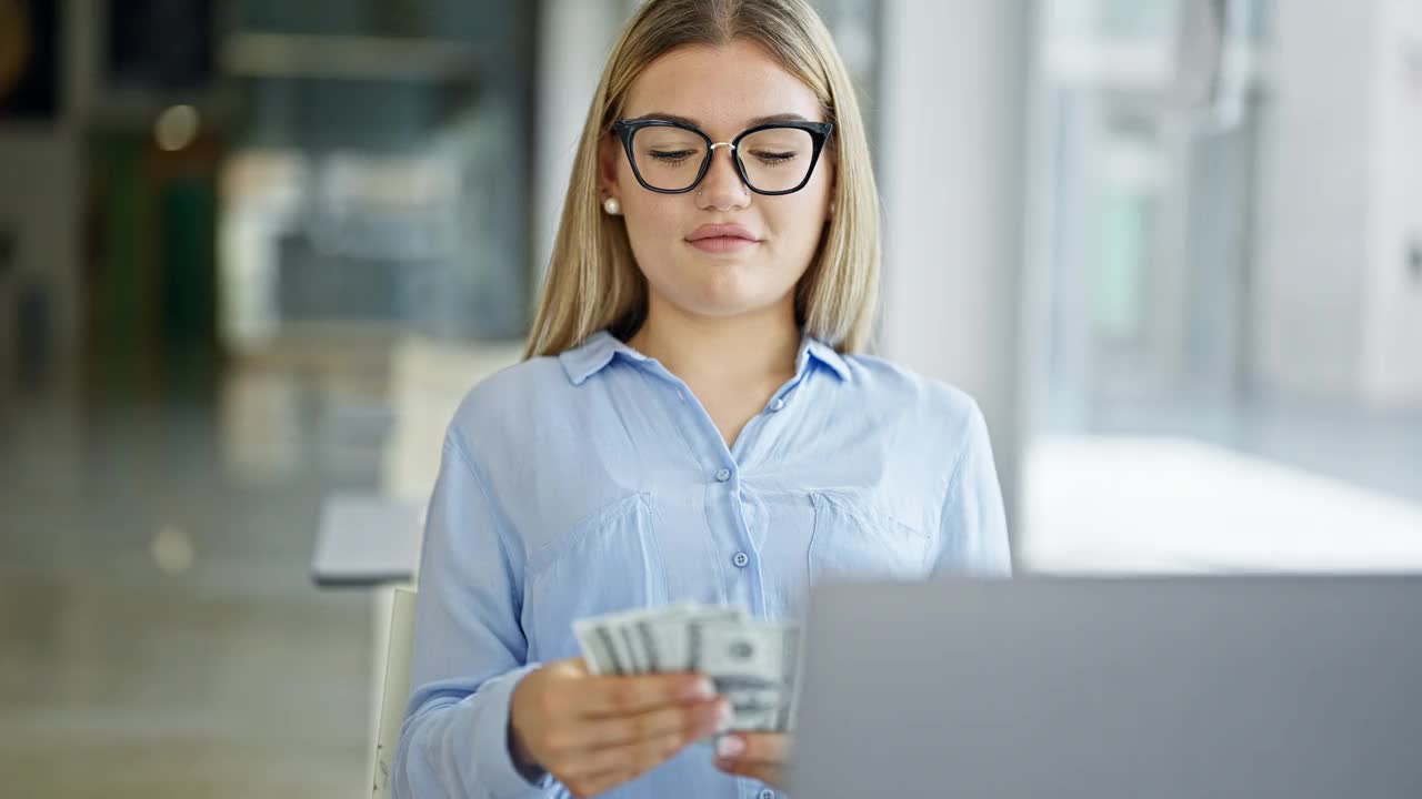 年轻的金发女商人在办公室用笔记本电脑计算美元视频素材