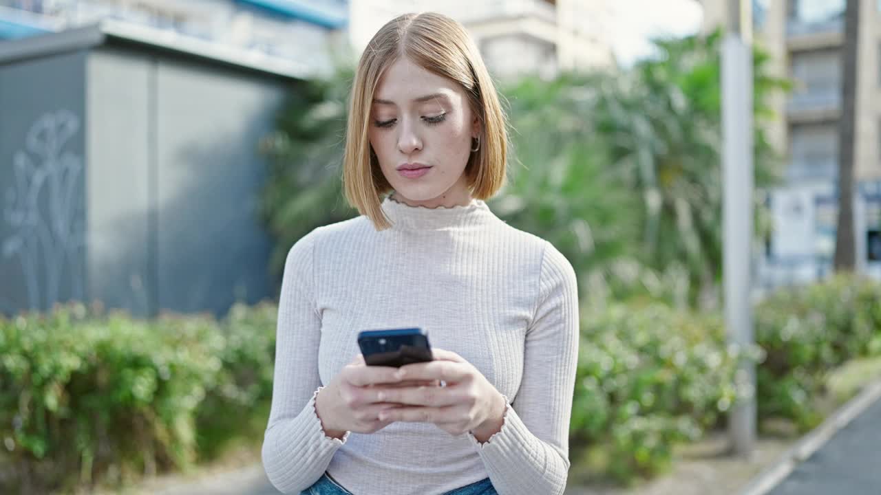 年轻的金发女子在公园里用智能手机自信地微笑着视频素材