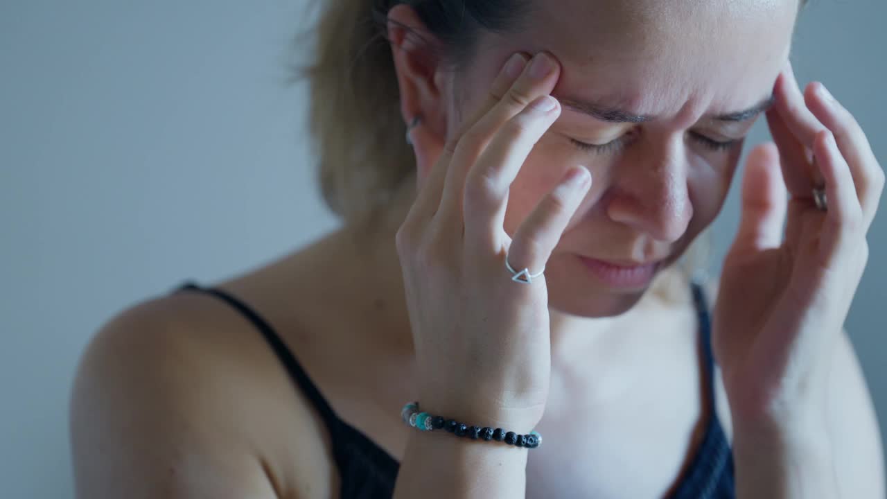 一个女人闭着眼睛坐着，因为头痛而揉着太阳穴视频素材