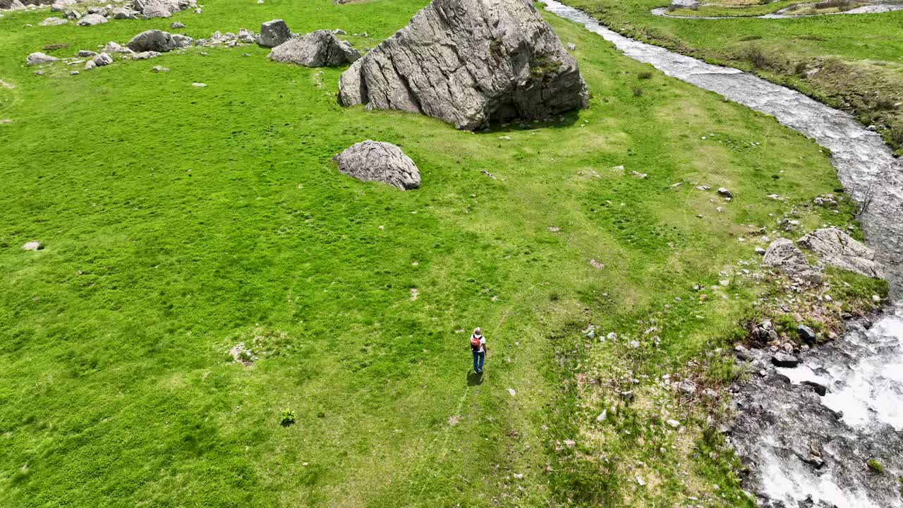 成熟的徒步旅行者走过小溪旁的山间草地视频下载