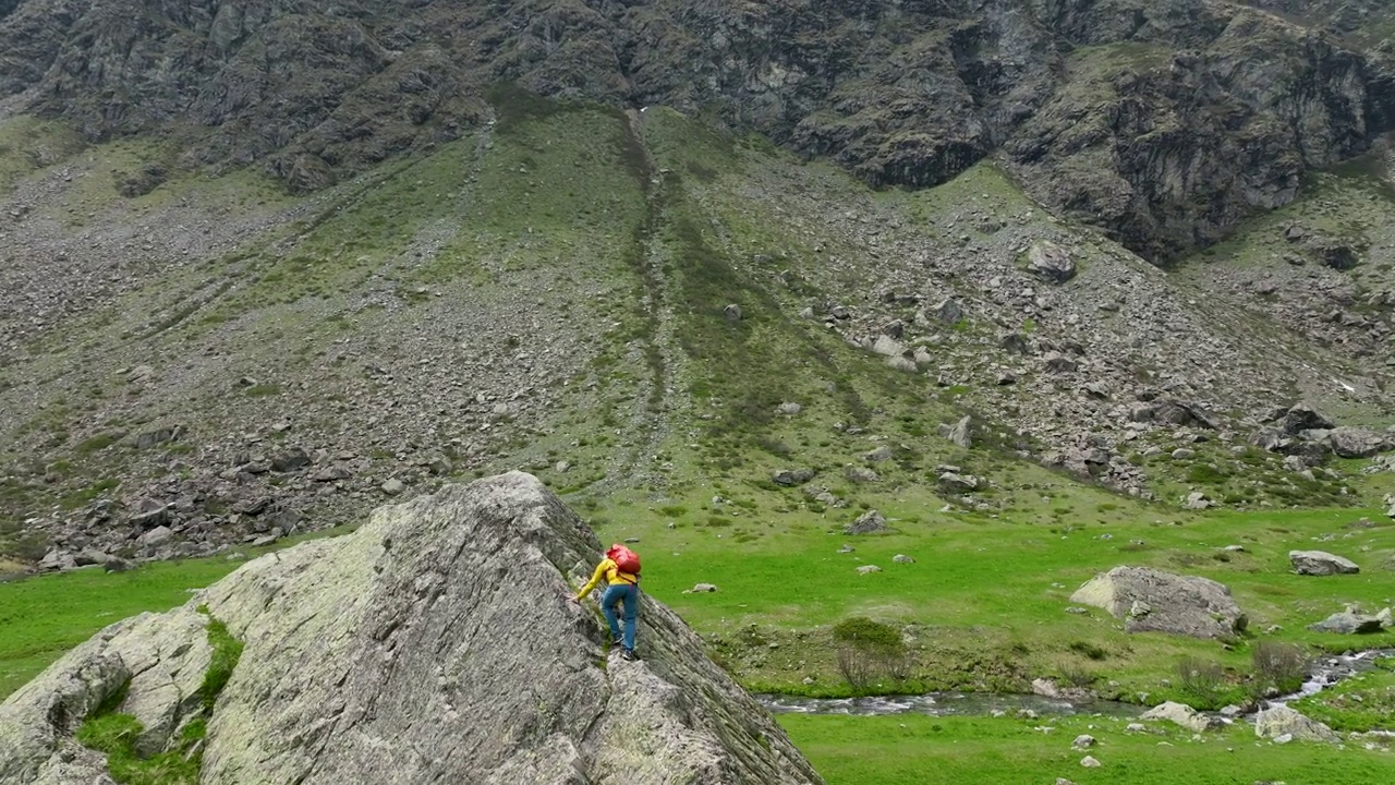 成熟的徒步旅行者爬上草地上的巨石，欣赏崎岖的山景视频下载