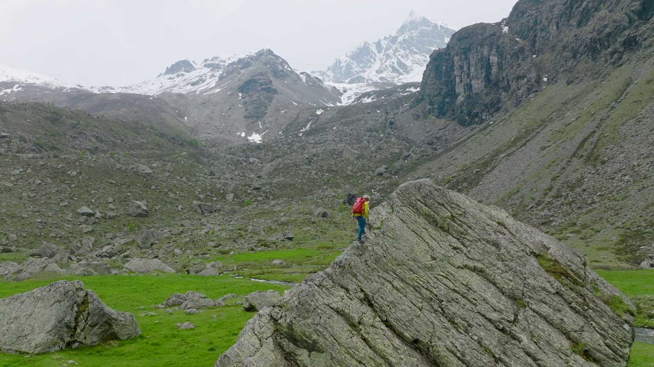 成熟的徒步旅行者爬上草地上的巨石，欣赏崎岖的山景视频下载