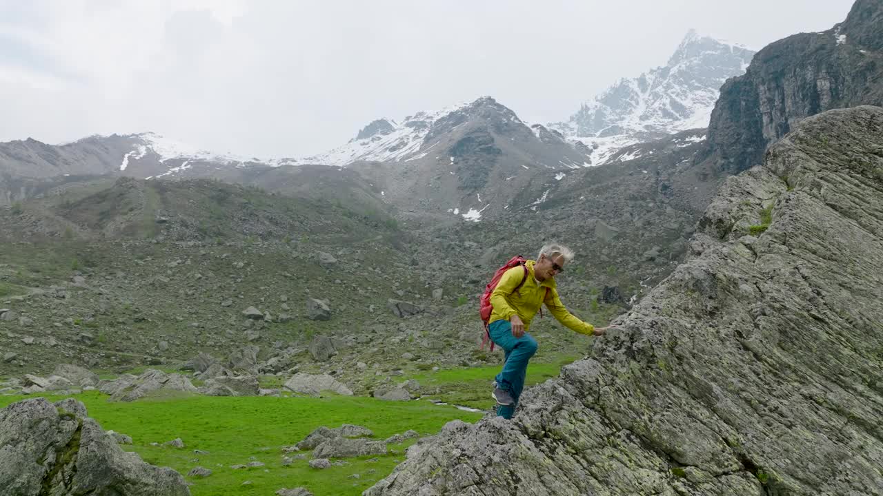 成熟的徒步旅行者爬上草地上的巨石，欣赏崎岖的山景视频下载