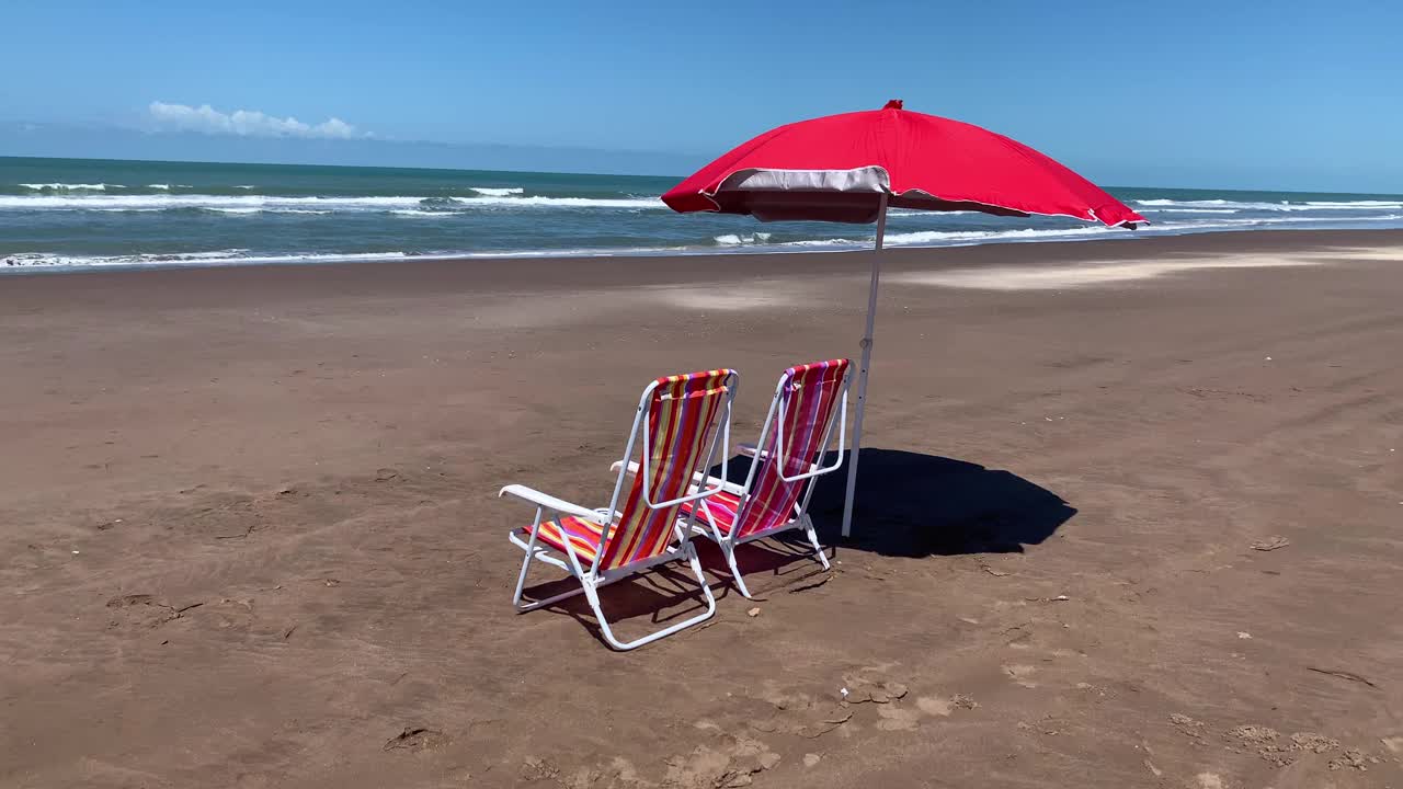 两把空沙滩椅和一把伞放在海边的沙滩上。夏季概念，视频4k视频素材