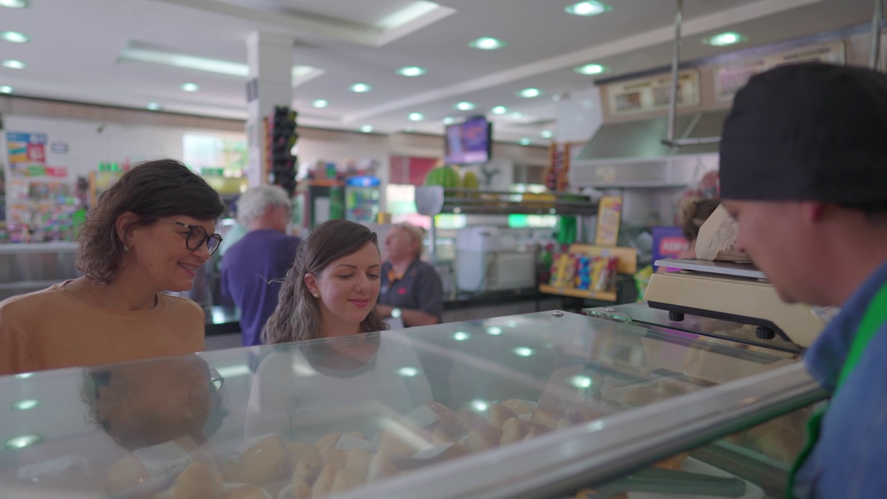 熟食店员工，在柜台后协助顾客。两个女人隔着玻璃看食物，在自助餐厅挑选食物视频素材