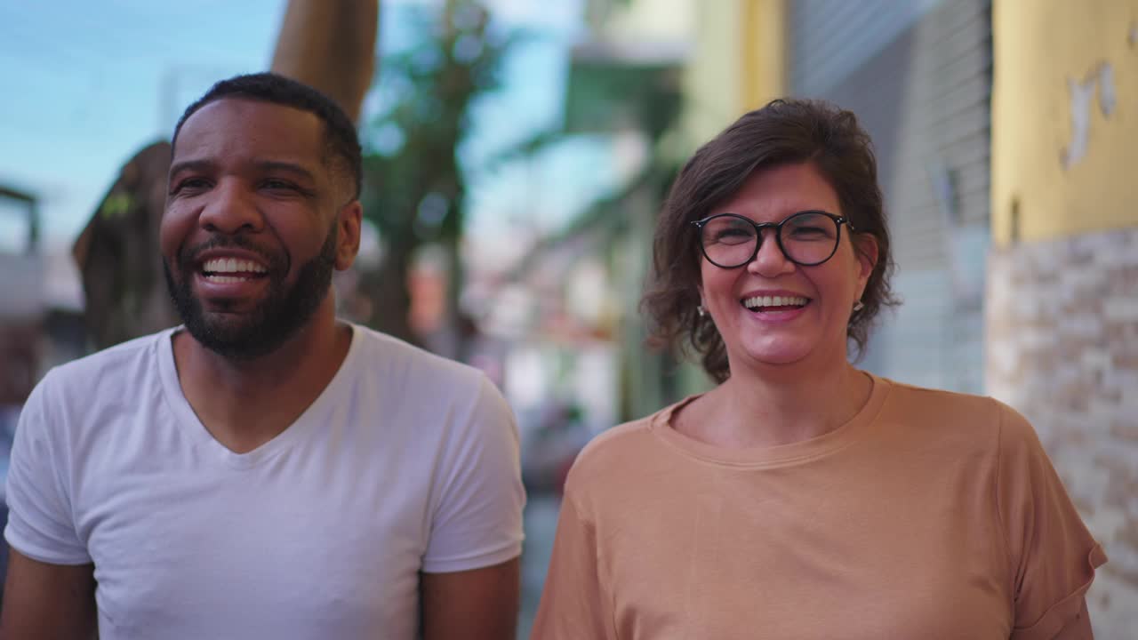 Happy mature caucasian woman walking with an African American man in sidewalk while laughing and smiling together. Joyful Diverse People视频素材