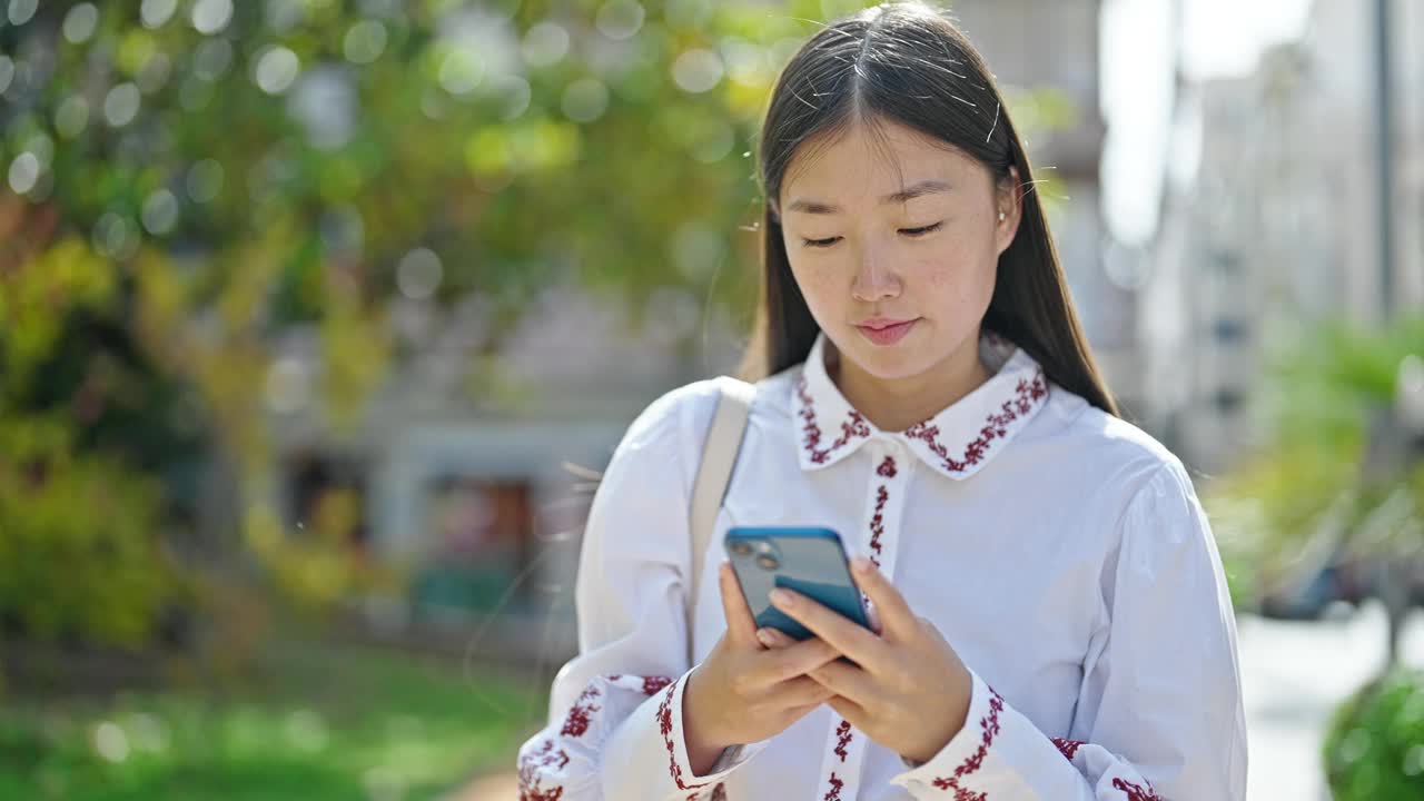 年轻的中国女子在公园用智能手机微笑视频素材