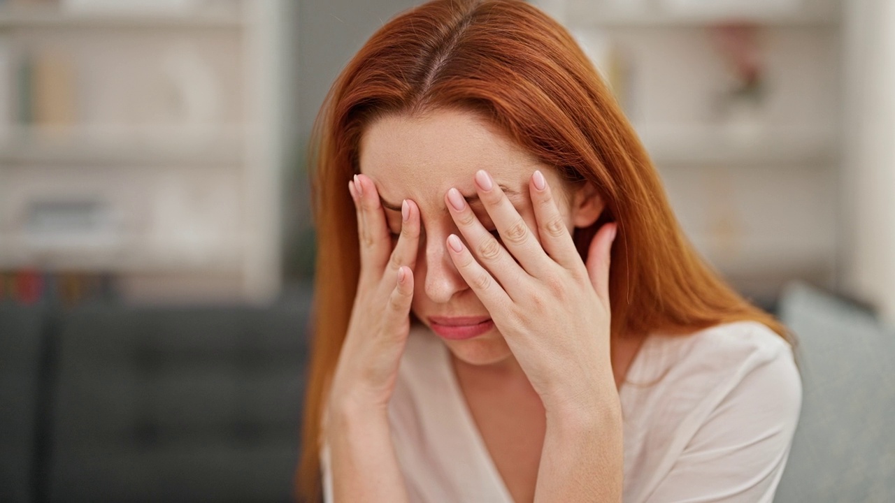 年轻的红发女人坐在家里的沙发上视频素材