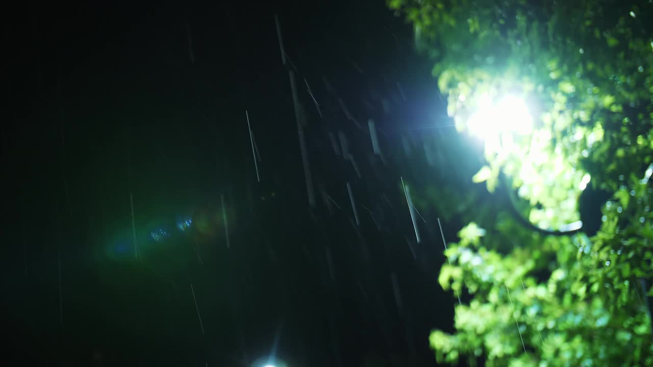 路灯。雨下降。夜里下雨了。光雨。水坑与灯光反射在城市人行道上。路灯。雨滴与路灯。特写镜头。视频素材