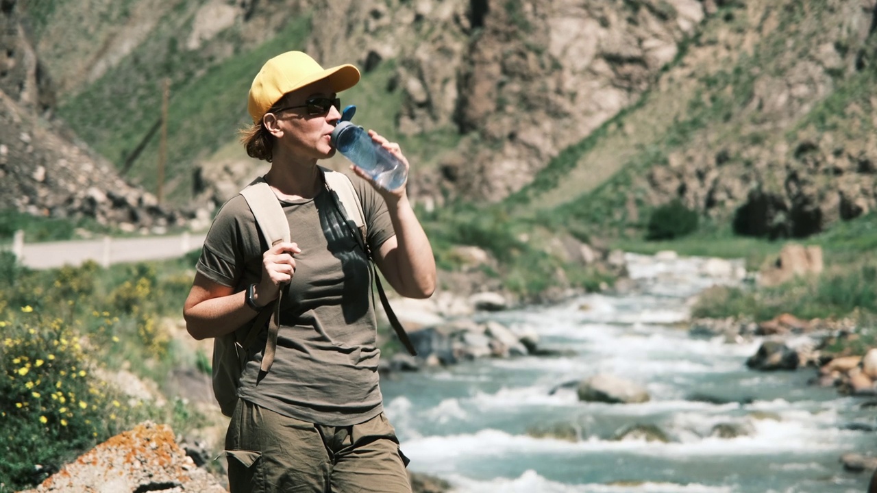 女背包客在峡谷里的山河边喝水视频素材