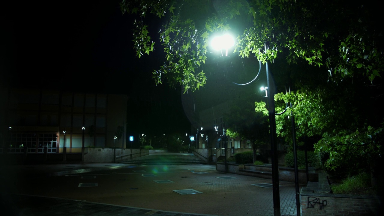 路灯。雨下降。夜里下雨了。光雨。水坑与灯光反射在城市人行道上。路灯。雨滴与路灯。视频素材