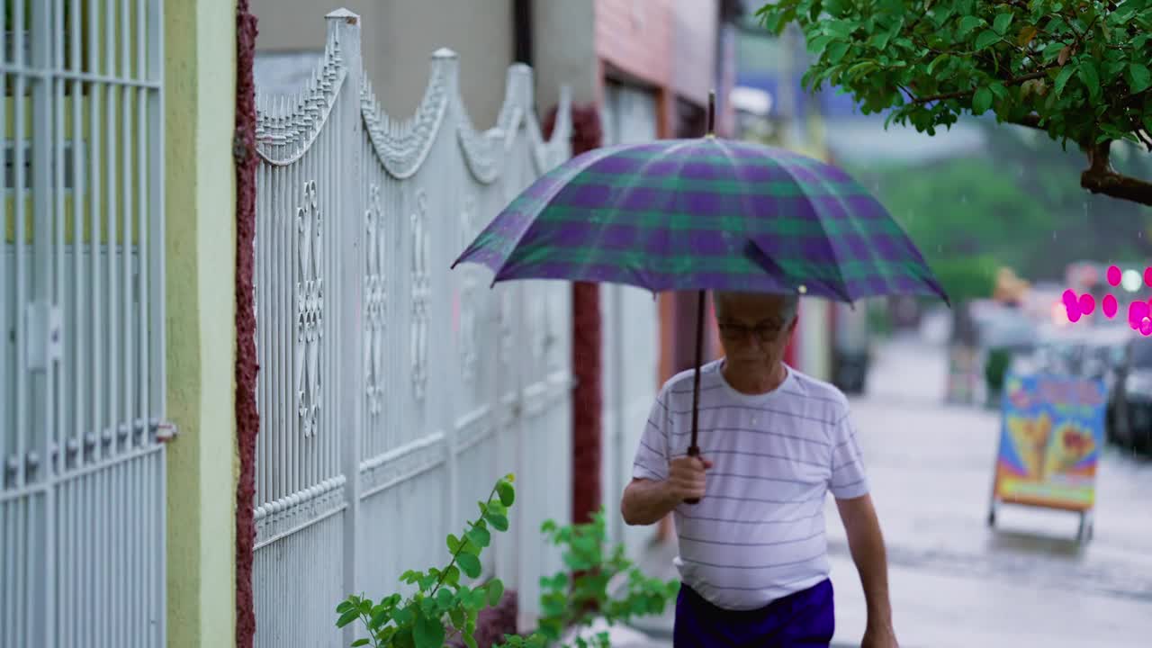 老人冒雨回家，撑开雨伞，锁好大门，走在人行道上视频素材