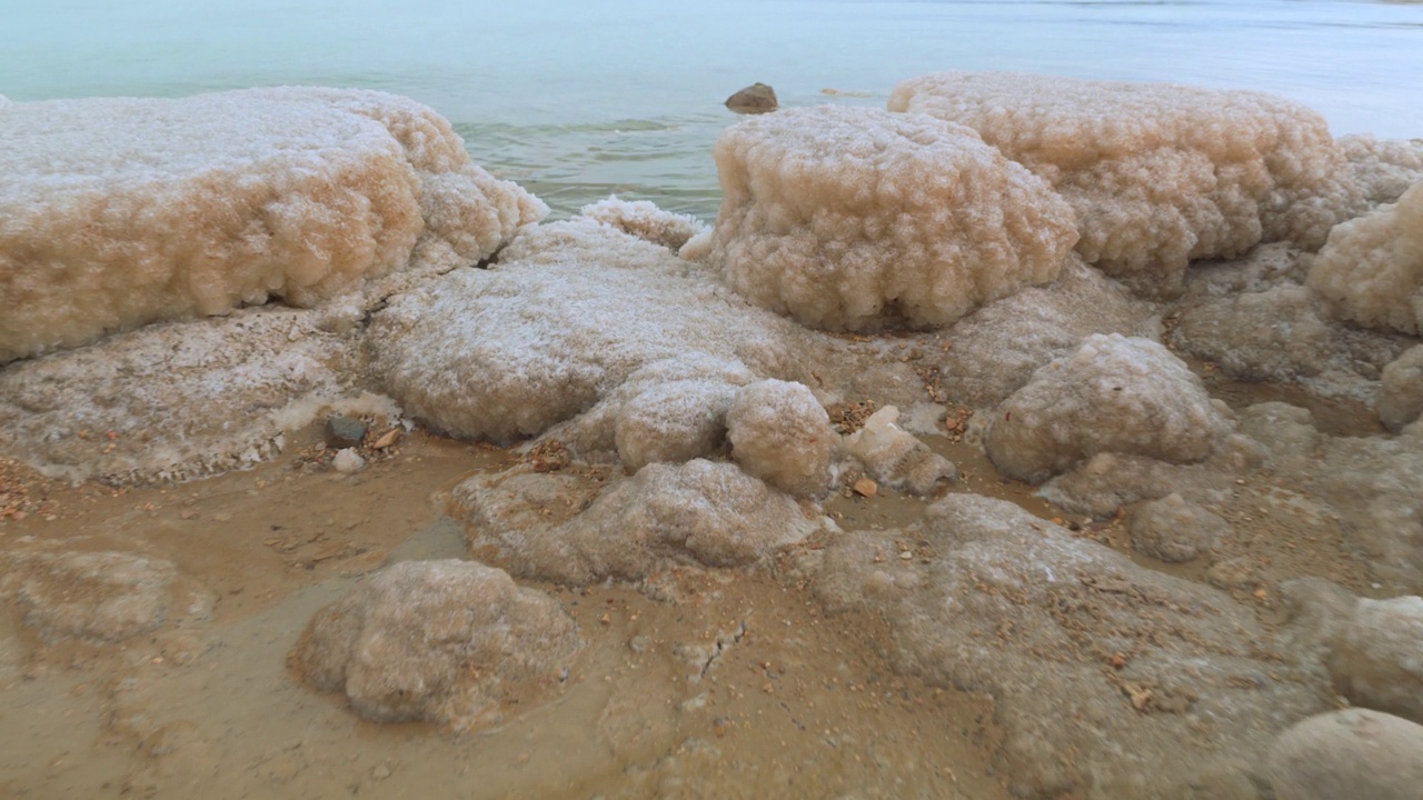 死海岸边覆盖着结晶盐的沙子，蓝绿色的海水靠近以色列艾因博克海滩的典型风景视频素材