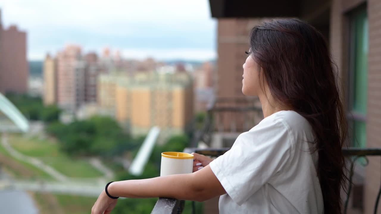 在阳台喝咖啡的亚洲年轻女子视频素材