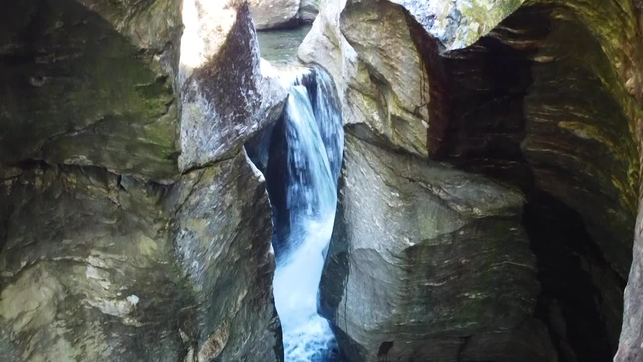 空中俯瞰岩石巨石峡谷，小瀑布进入蓝色的水域，雕刻成悬崖，周围是秋天的树叶和苔藓视频素材