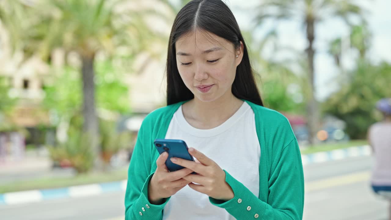 年轻的中国女子在公园带着胜利者的表情使用智能手机视频素材