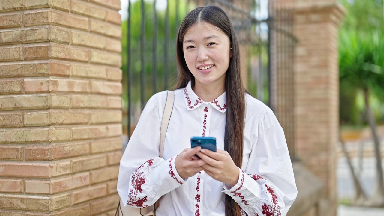 年轻的中国女子在街上用智能手机微笑视频素材