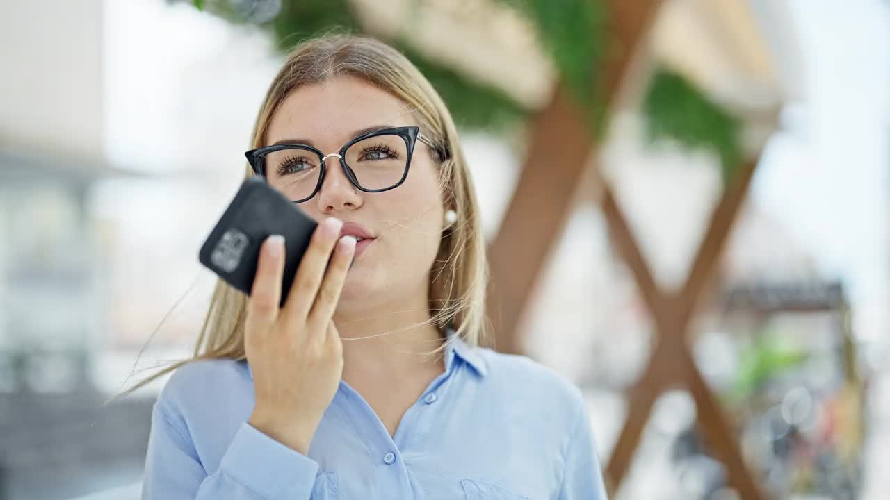 年轻的金发女商务工作者用智能手机发送语音信息，在街上微笑视频素材