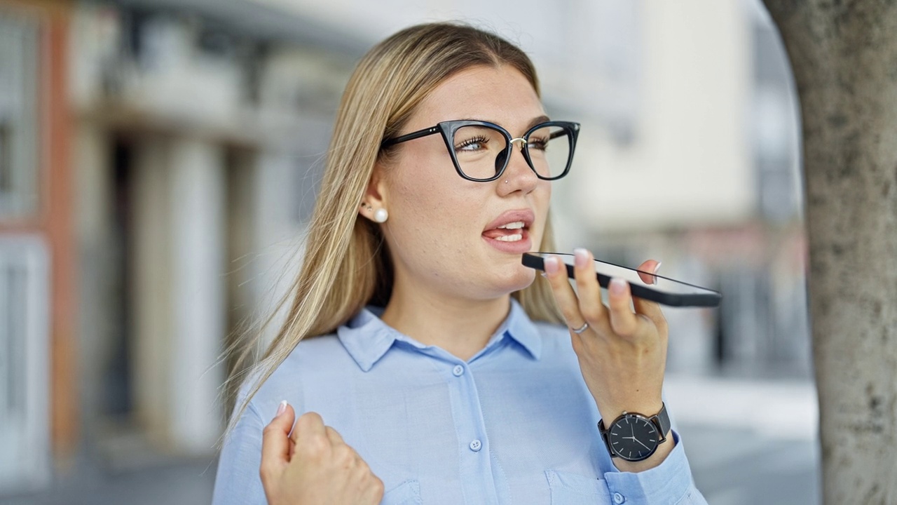 年轻的金发女商务工作者在街上用智能手机发送语音信息视频素材