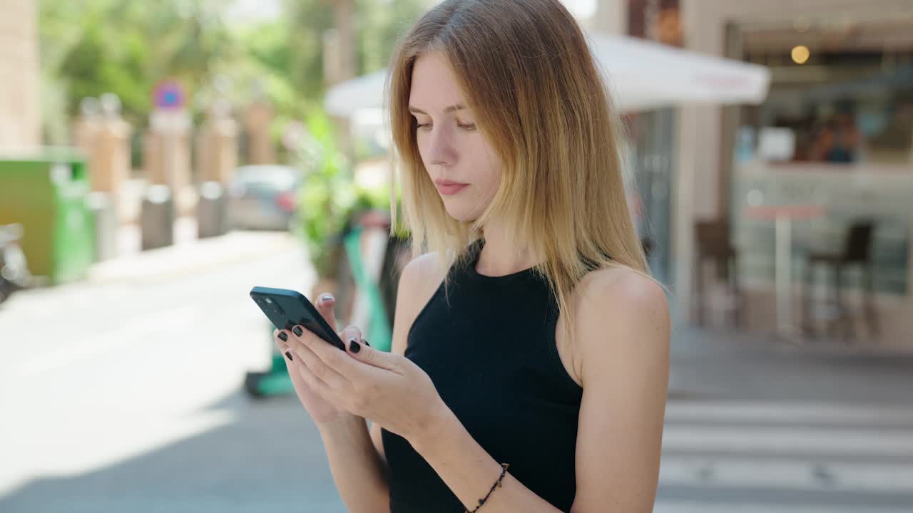 年轻的金发女子微笑着自信地在街上进行视频通话视频素材