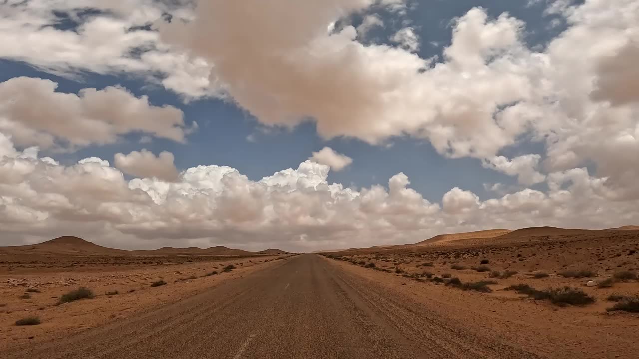 沿着干旱的沙漠公路行驶，蓝天白云。第一人称驾驶员视角视频素材