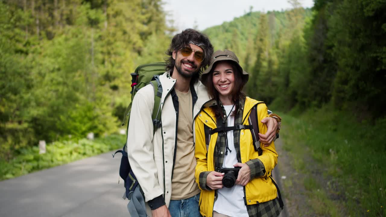 一男一女游客穿着特殊的徒步旅行服装，在山林的背景下拿着相机摆姿势视频素材