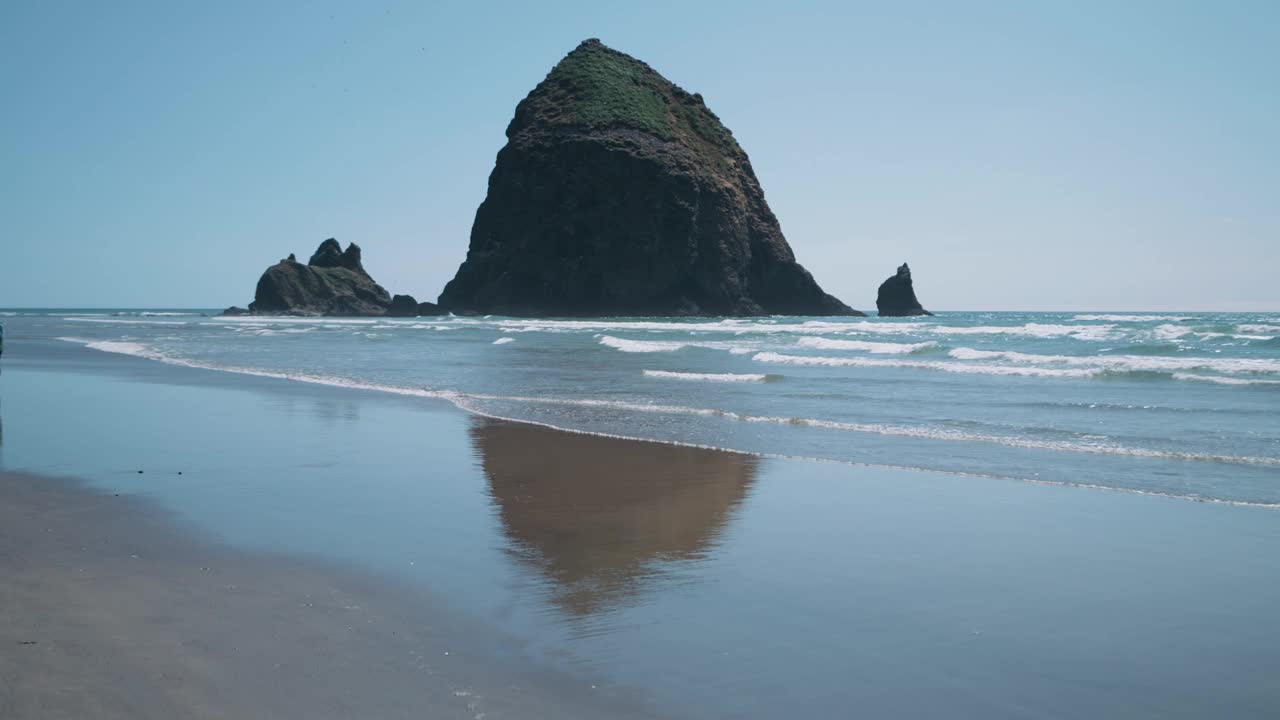 蓝蓝的天空下，沙滩上长满苔藓的岩石形成，海浪飞溅视频素材