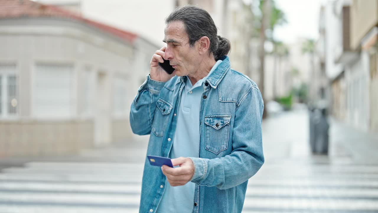 中年男子手持信用卡在街上用智能手机争吵视频素材