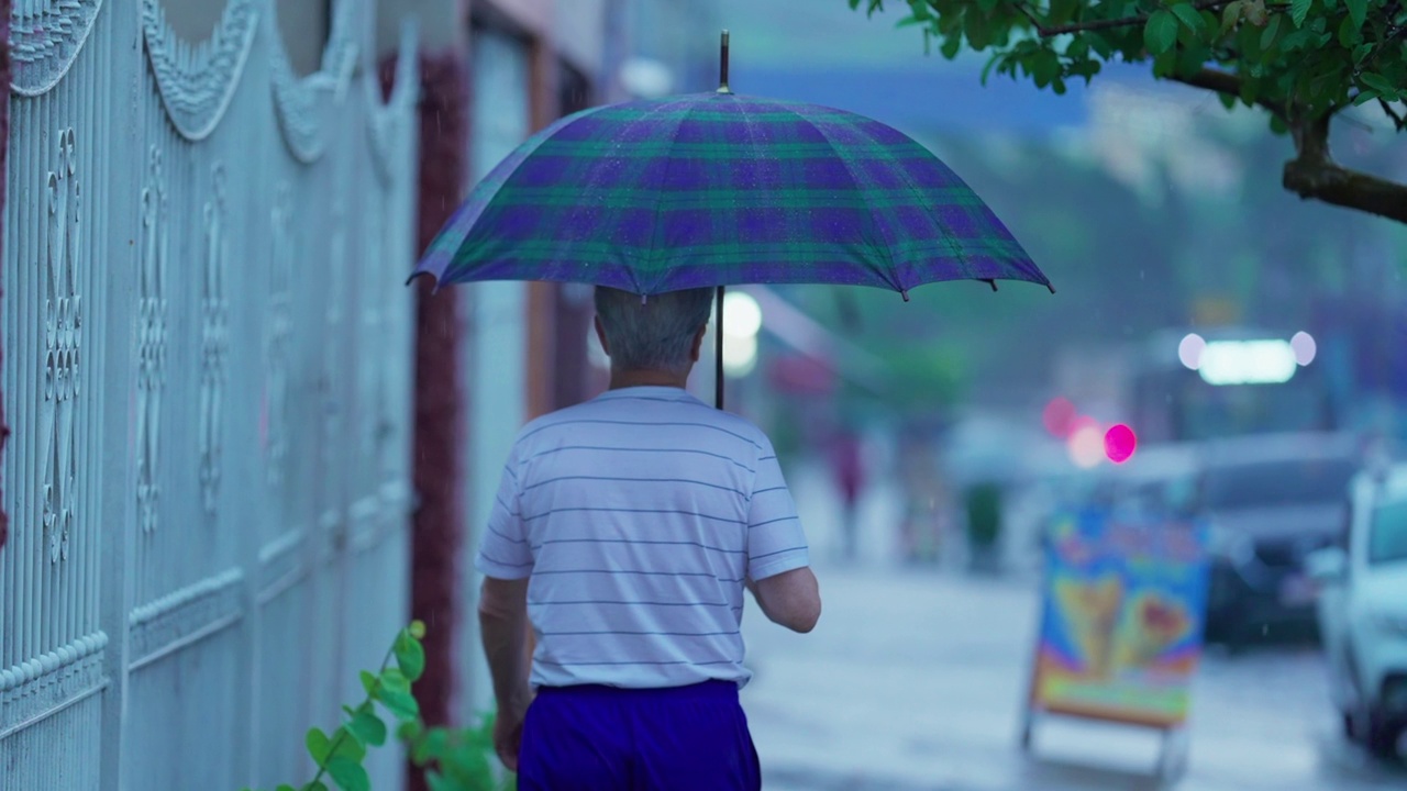 后面的人在雨中打着伞走着。老人在雨中散步视频素材