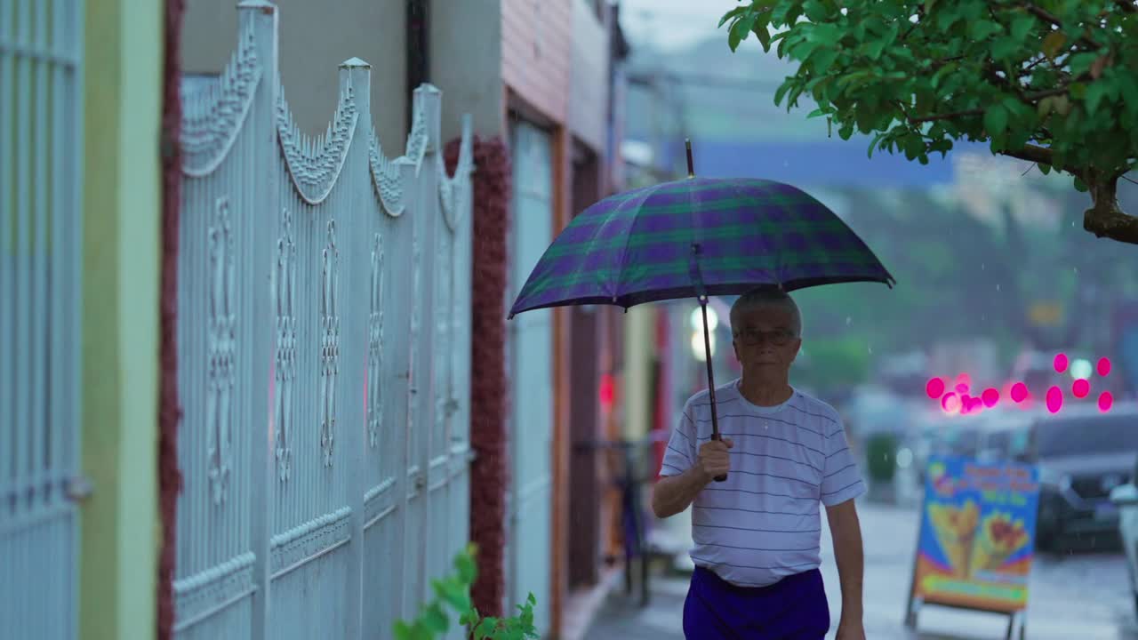 年长的白人男子在雨中打着伞在街上散步视频素材