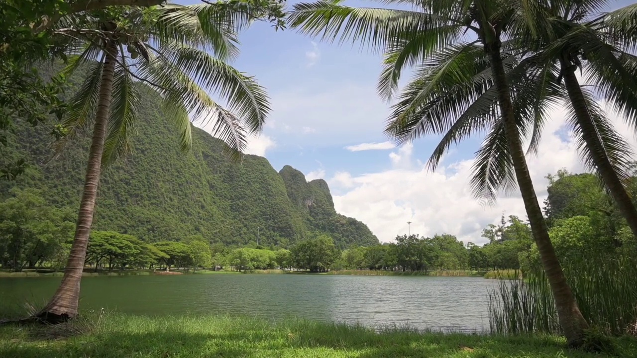 漫步在草坪上，欣赏山谷中天然池塘的美景，夏日蓝天多云。视频素材