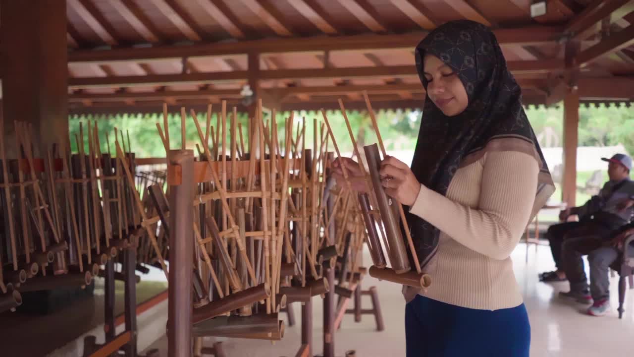 女穆斯林微笑着摇晃着angklung，这是一种来自爪哇的传统印尼乐器，由竹子制成。通过摇动来发出声音。视频素材