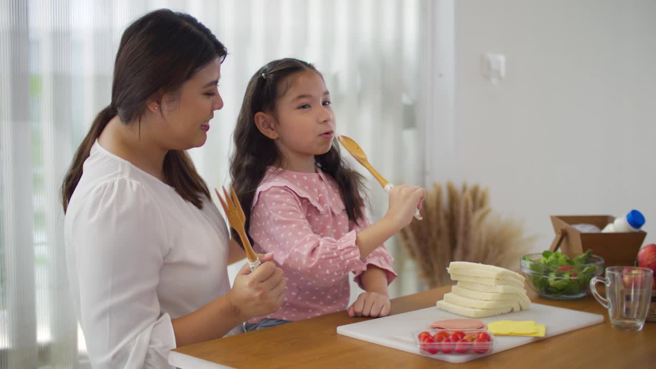 快乐的年轻母亲和女孩一起做健康的自制三明治和沙拉视频素材