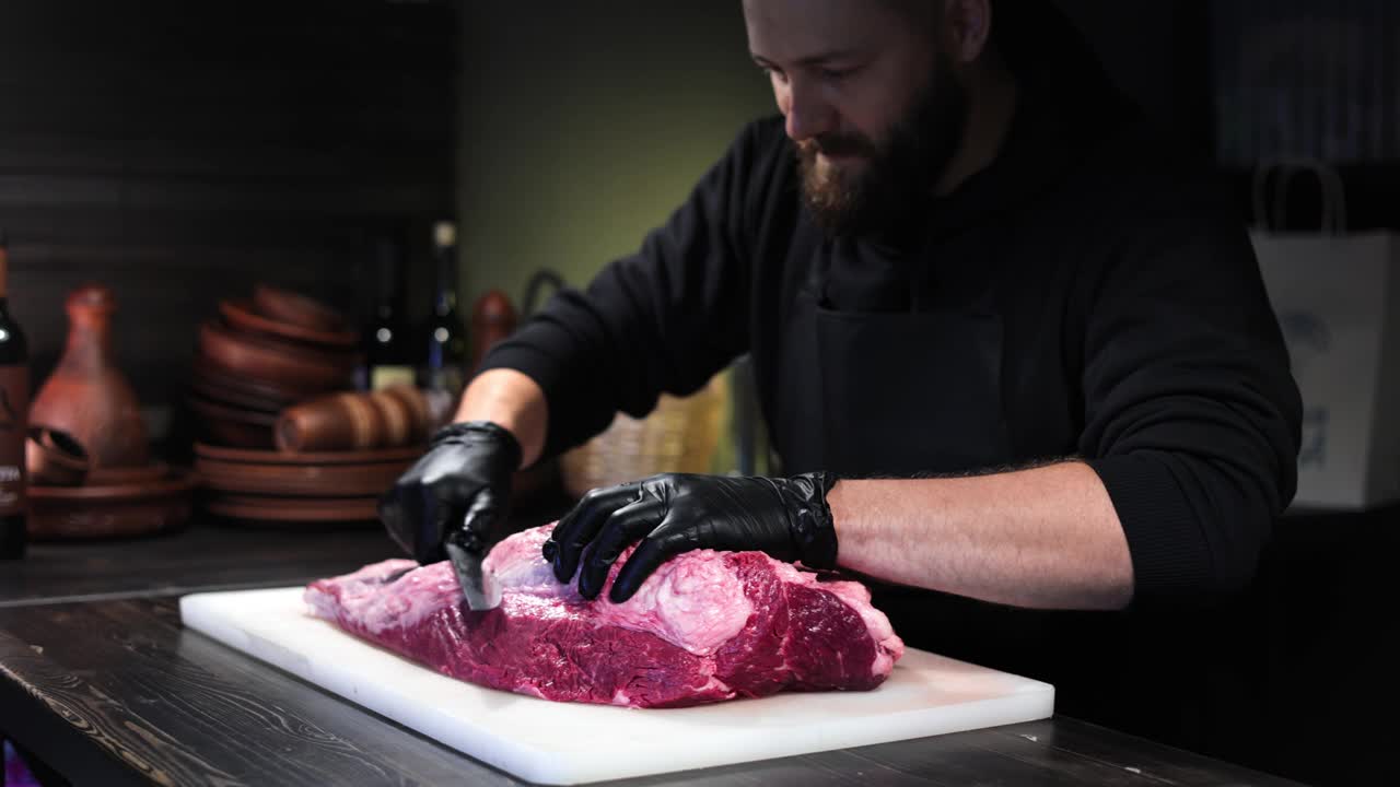 男厨师在餐厅厨房用锋利的刀切大块的生红肉牛排视频素材