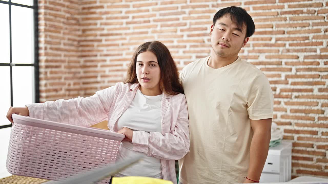 一男一女夫妇微笑着自信地捧着洗衣篮里的衣服视频素材