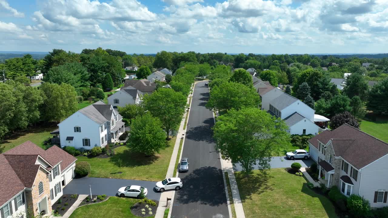 夏天的美国社区。住宅开发街道上的空中飞行，两旁是成熟的树木和大型家庭住宅。视频素材