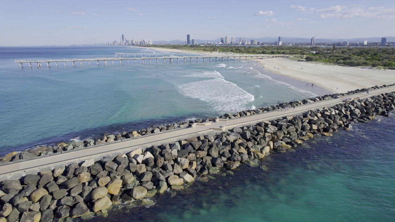 海浪涌向沙质地带的黄金海岸-捕鱼码头和海堤。-空中回拉视频素材