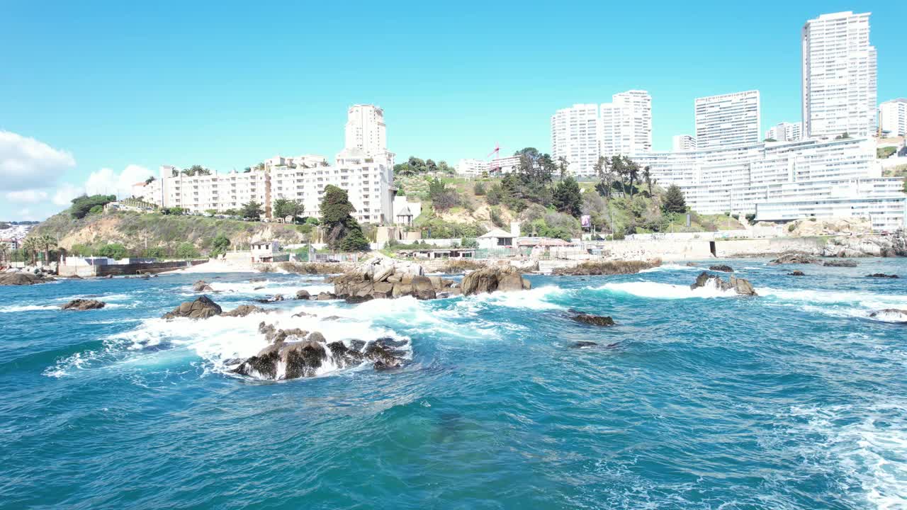 智利，海浪冲击Viña del Mar的海岸岩石，背景是建筑物和码头视频素材