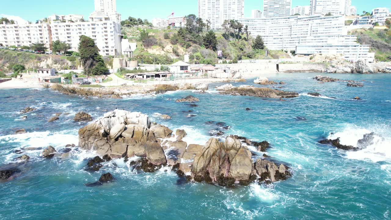 智利，海浪冲击Viña del Mar的海岸岩石，背景是建筑物视频素材