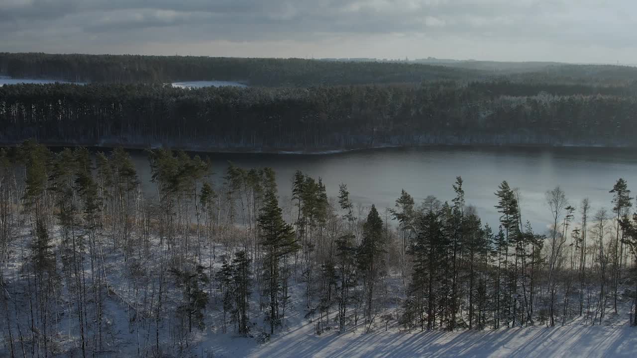 鸟瞰白雪覆盖的树梢，森林冬日平静的湖面。在美丽宁静的冬湖上，飞过令人惊叹的白松林。飞越冰雪覆盖的冬季景观。视频素材